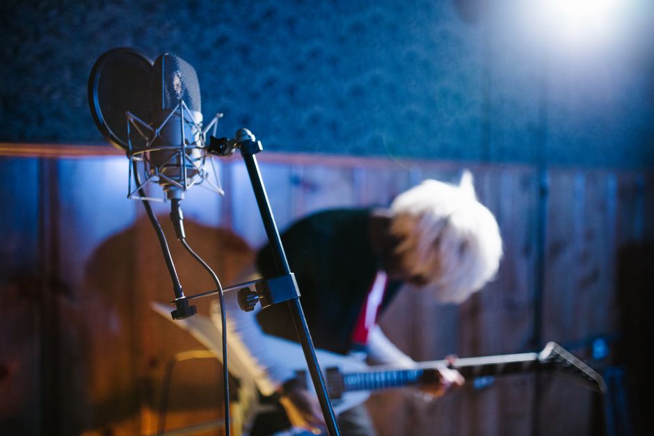 Blurred guitarist in a vibrant studio, mic in foreground capturing dynamic energy.
