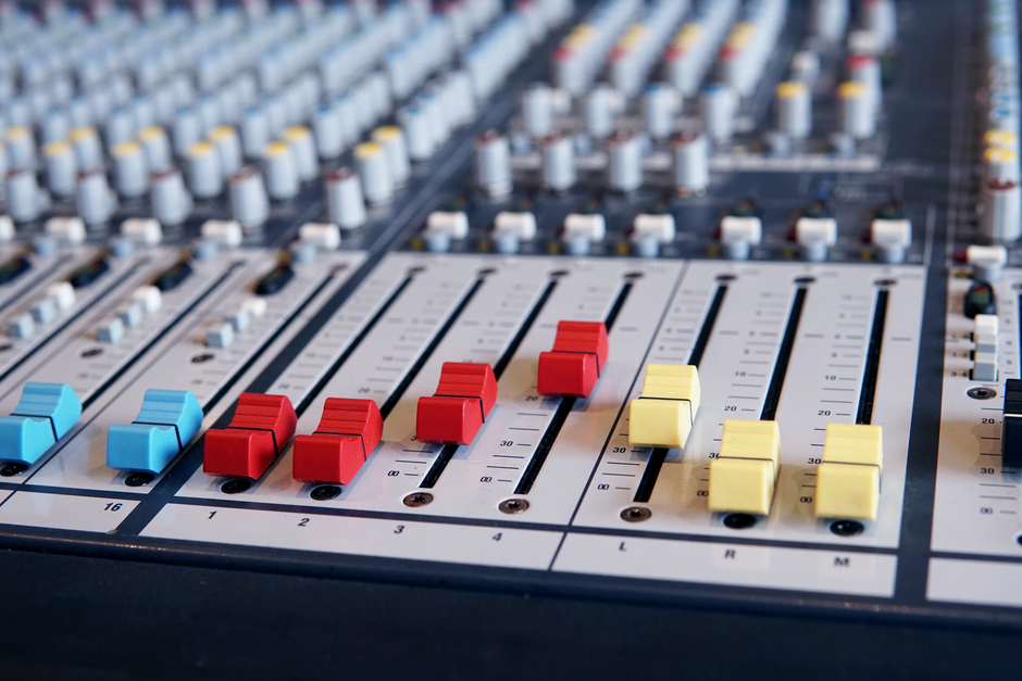 Detailed shot of a mixing console with vibrant red, blue, and yellow faders.